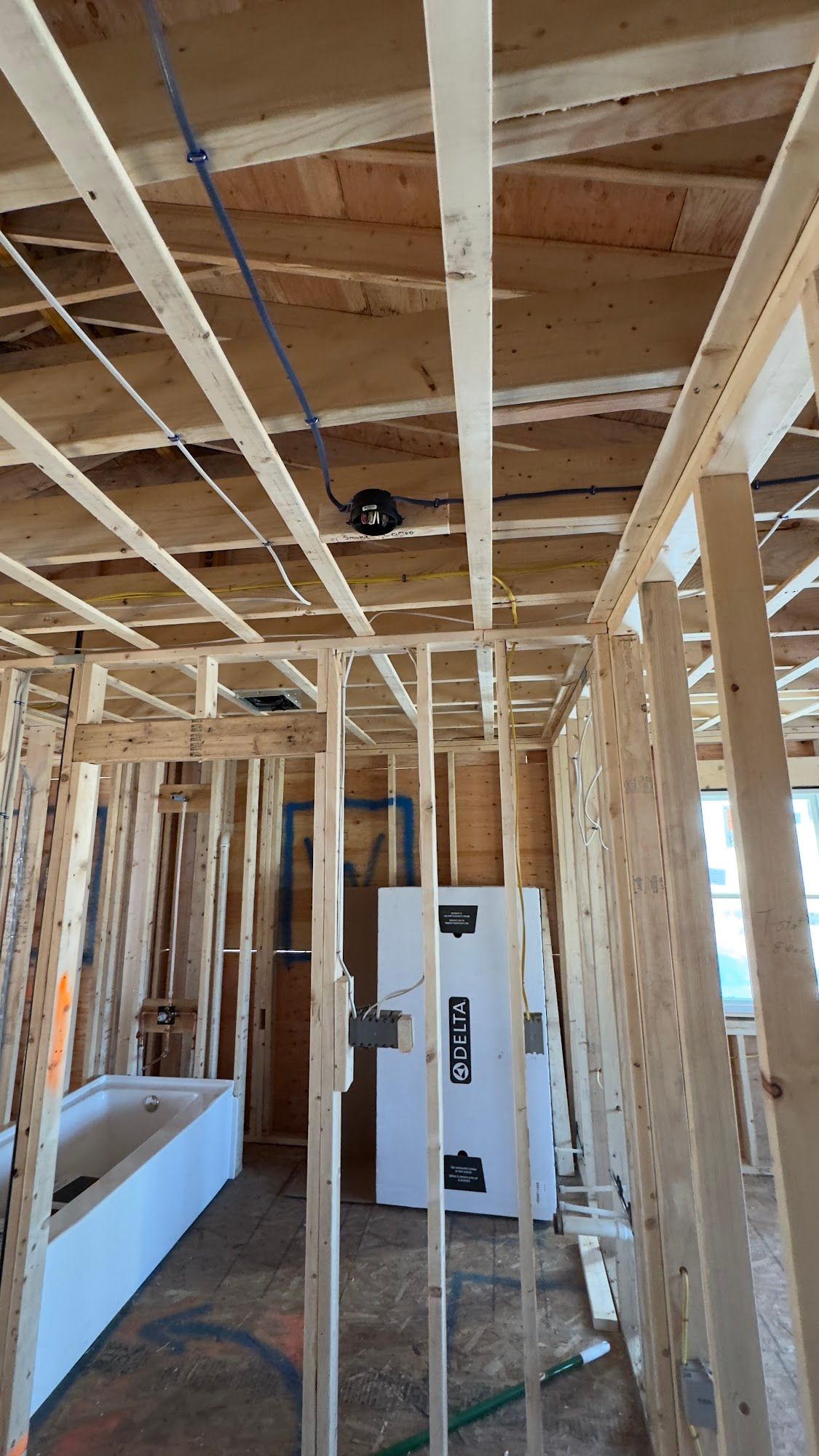 Interior view of a building under construction, showing wooden framing, electrical wiring, and a white appliance.