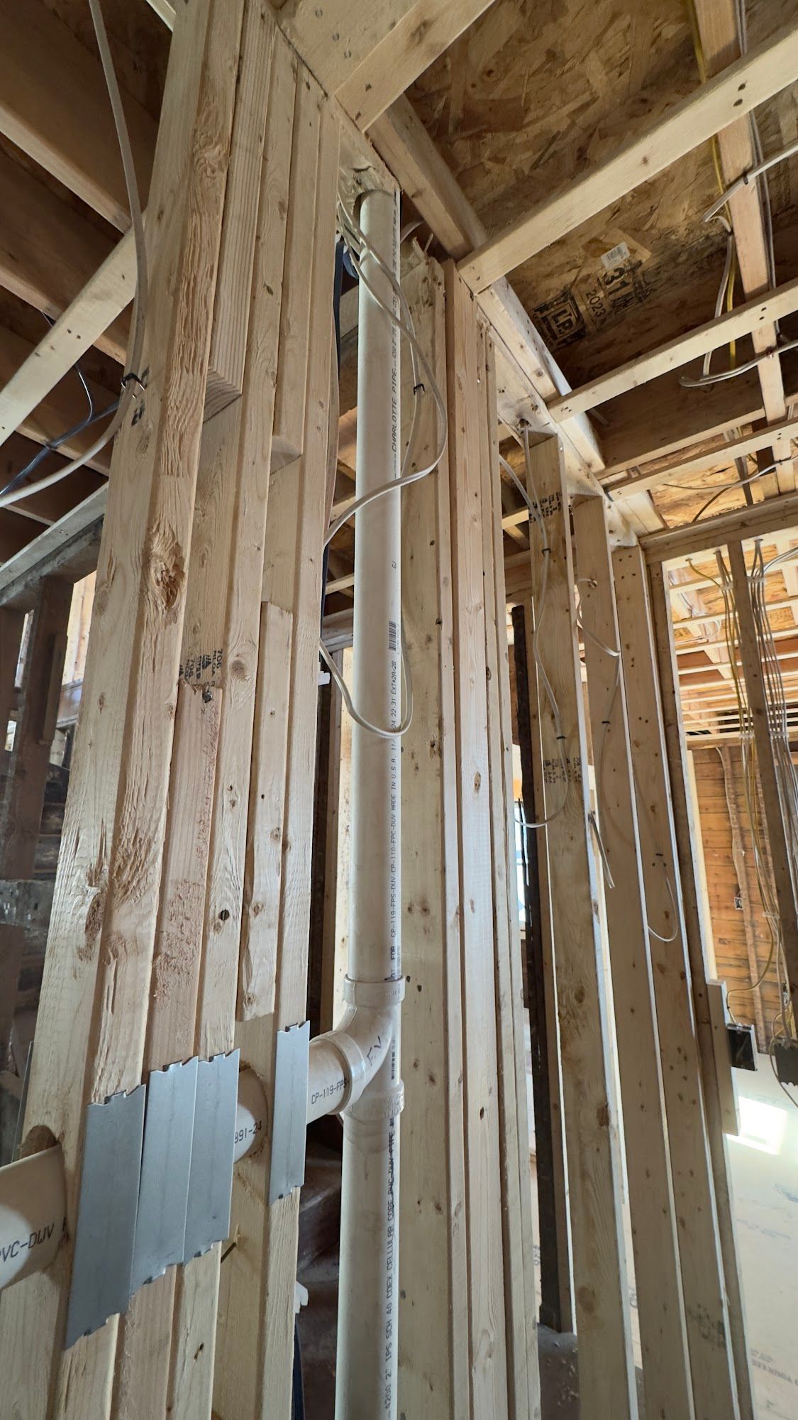 Interior view of a building under construction. White PVC pipe runs vertically through wooden beams.