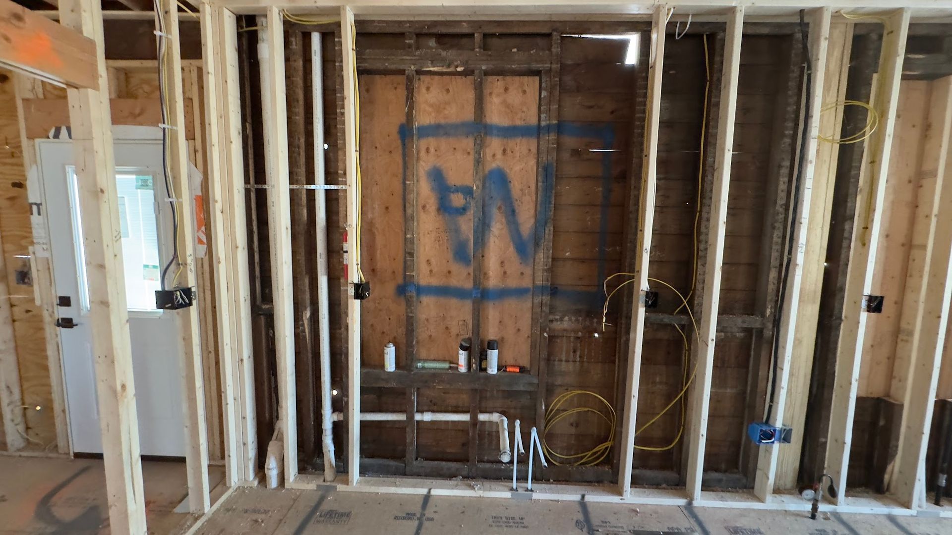 Interior wall framing with exposed electrical wiring and plumbing in a new construction setting.