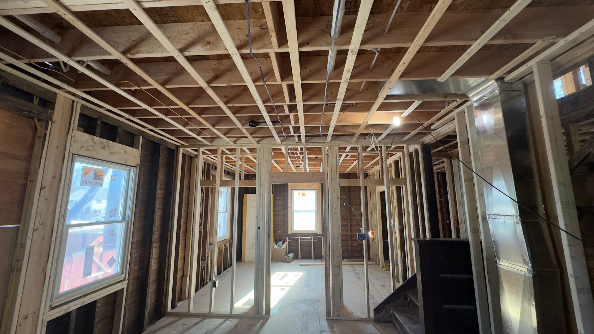 Interior room framing during construction, showing exposed wooden studs, windows, and ceiling beams.