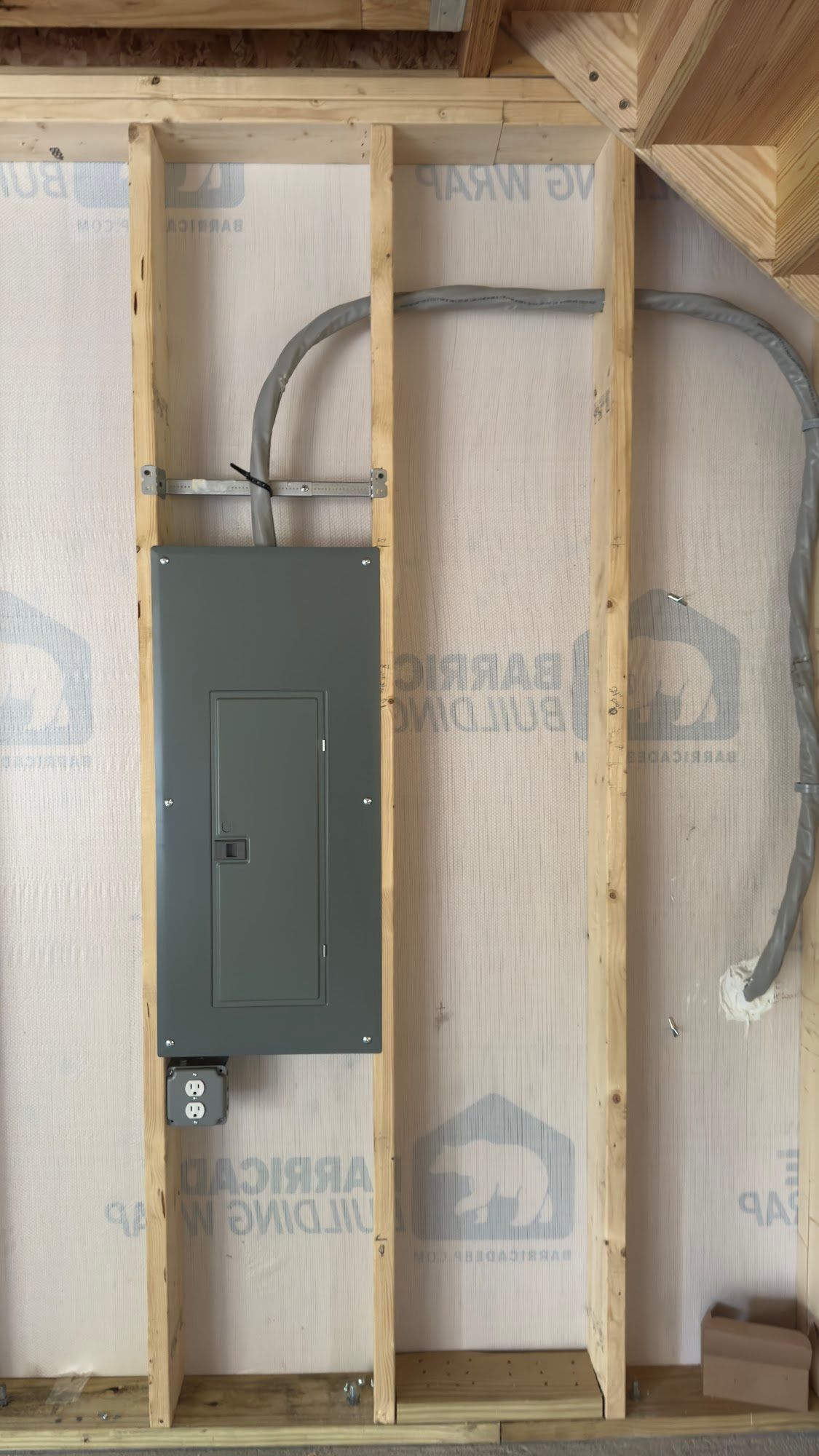 Electrical panel installed between wooden studs; conduit runs above and to the right.