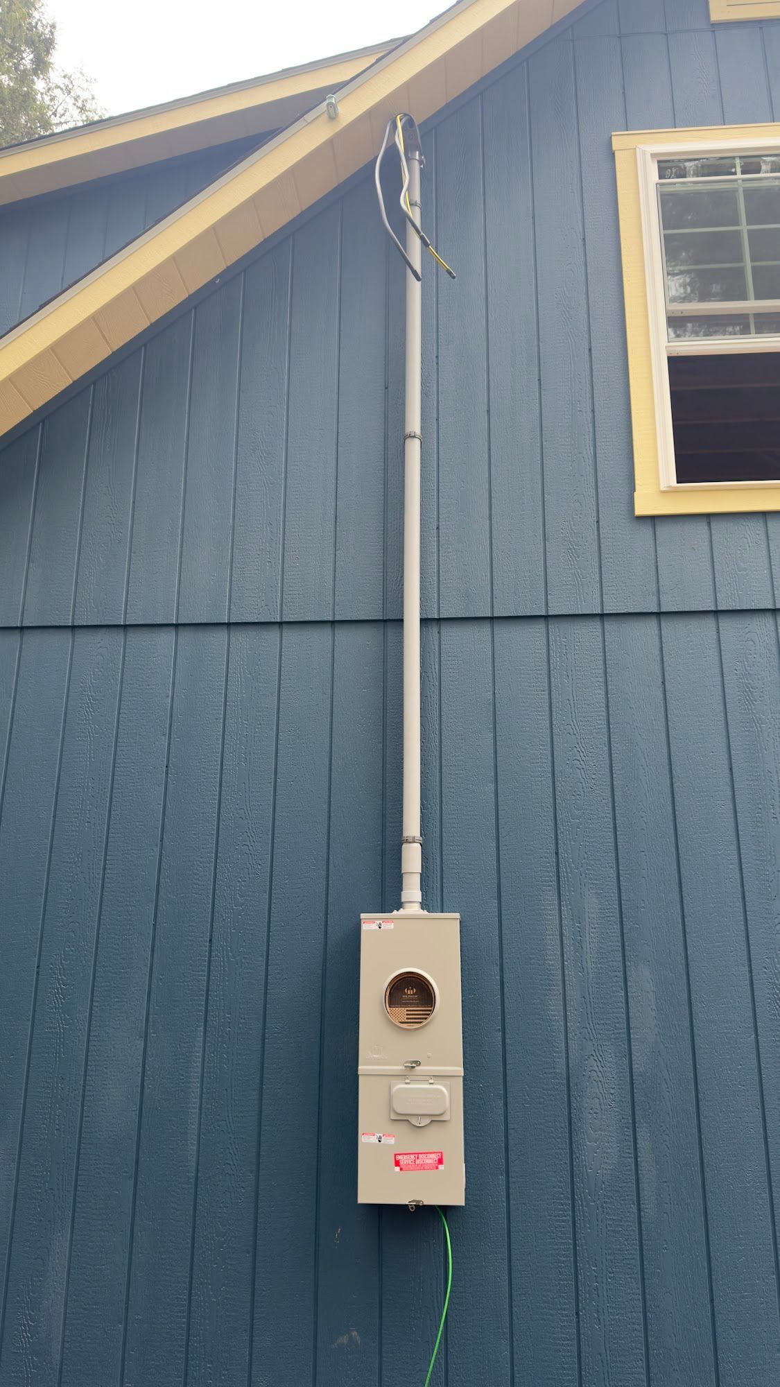 Gray electrical meter box mounted on blue house siding, with conduit running up to the roof.