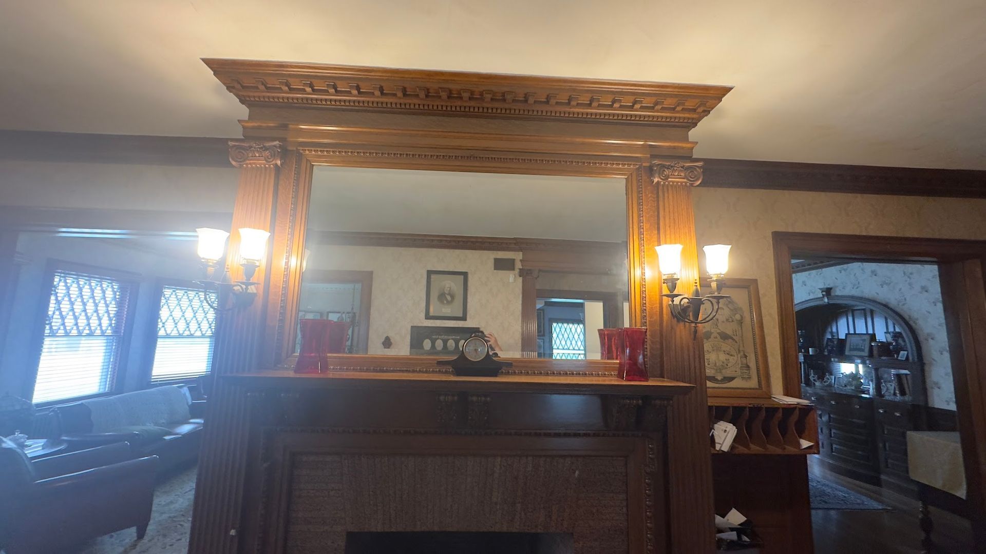 Ornate wooden fireplace with a large mirror, sconces, and a doorway.