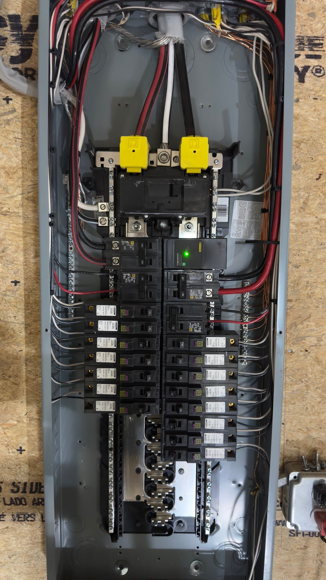 Electrical panel with numerous circuit breakers and wiring. Yellow-capped main breaker, various black and white wires.