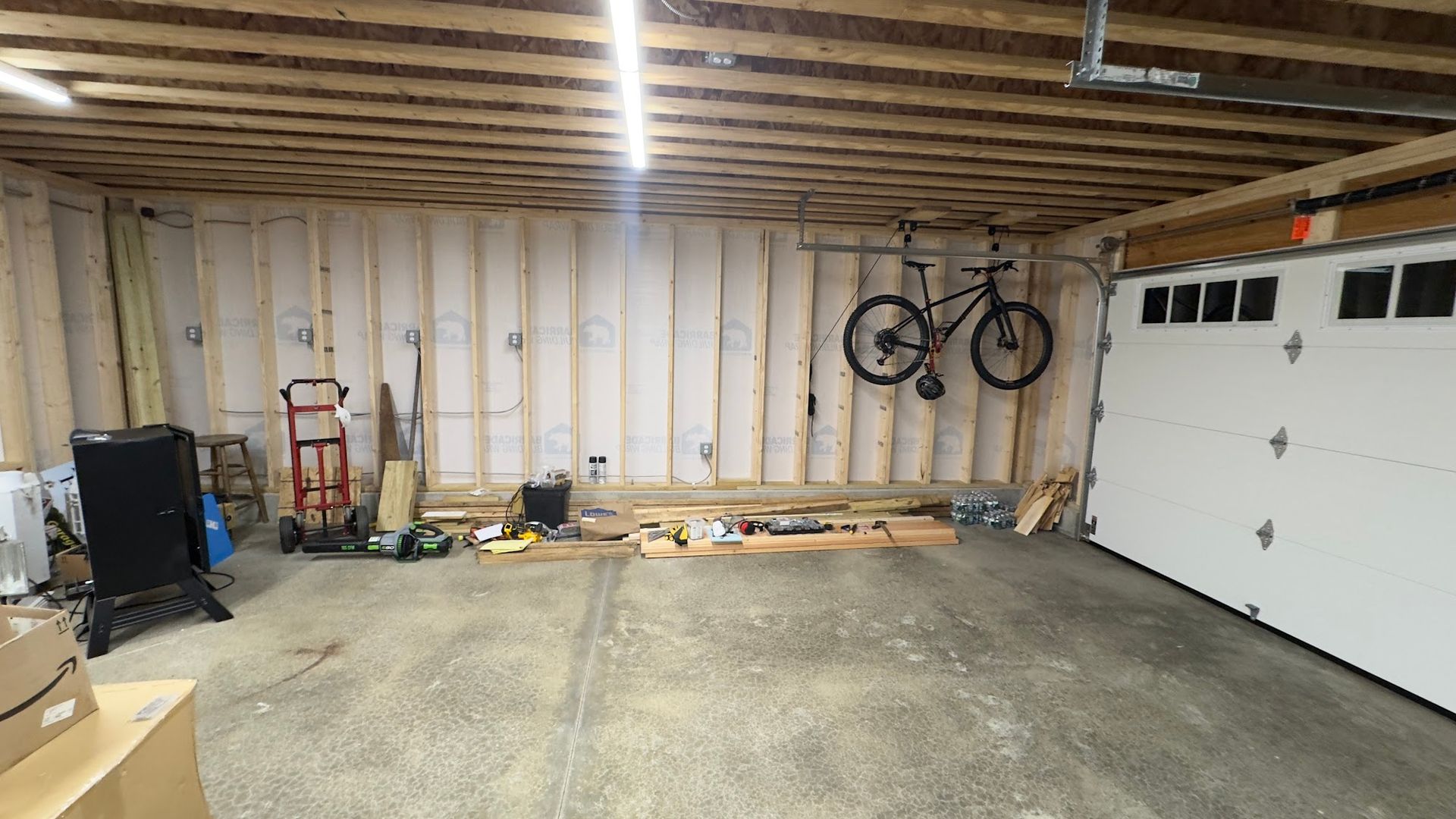 Garage interior with exposed framing, tools, and a bicycle mounted on the wall.