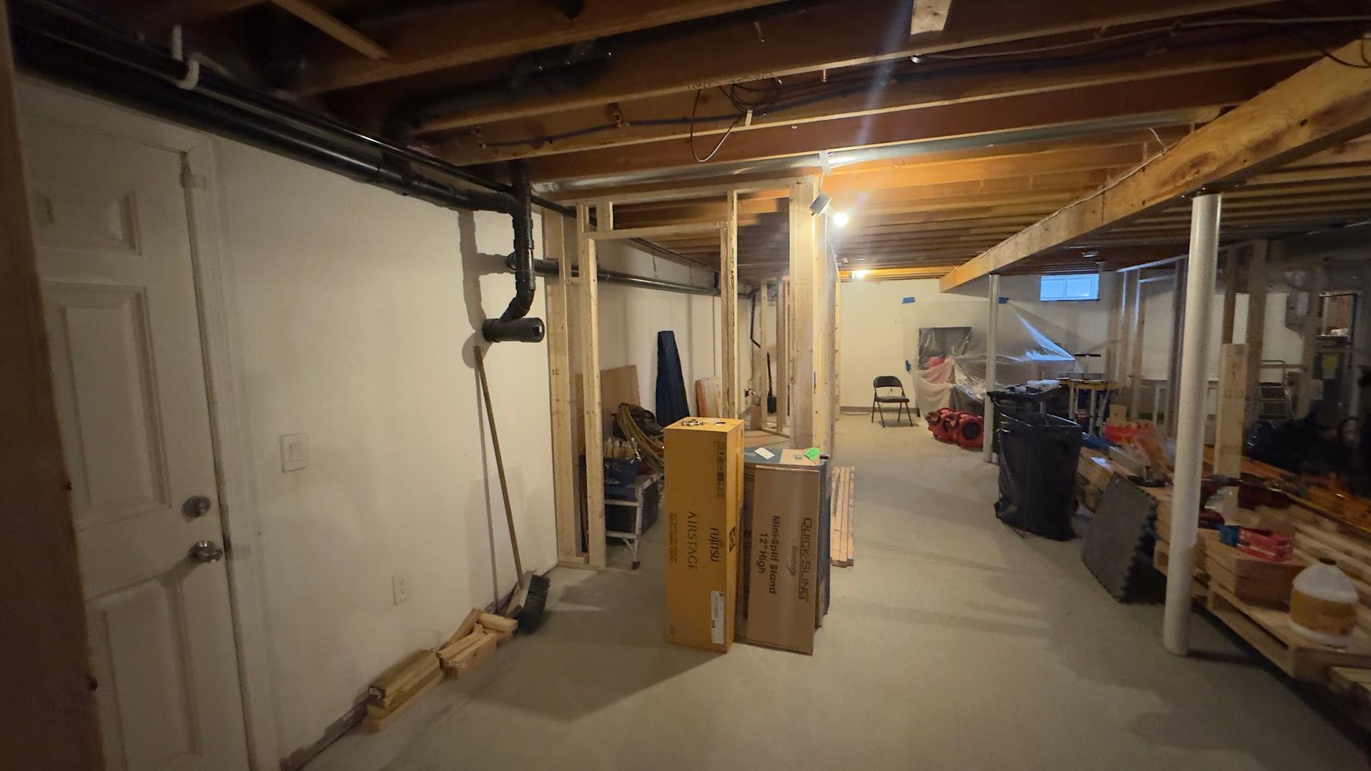 Basement renovation in progress; unfinished walls, exposed beams, plumbing, boxes, and door.