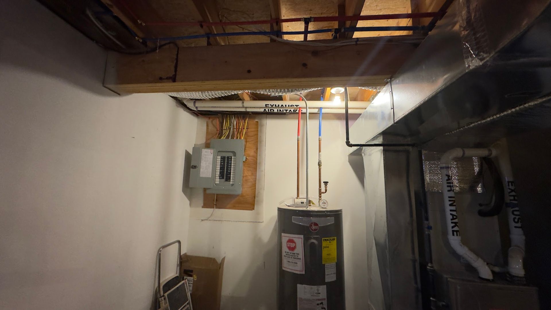 Basement with water heater, electrical panel, and exposed pipes near ceiling and HVAC system.