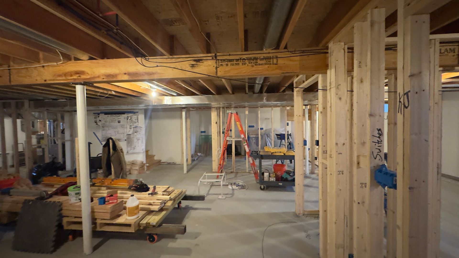 Basement renovation in progress. Exposed wood framing, unfinished walls, tools, and a ladder.