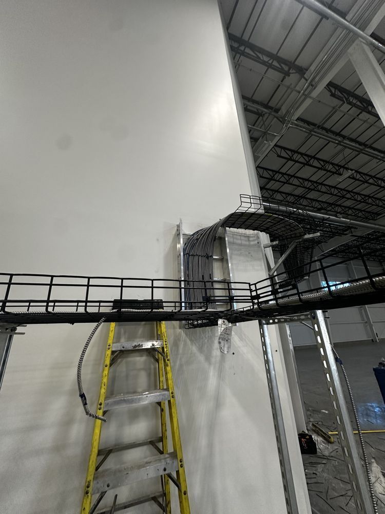 Yellow ladder next to a white wall with black cable trays and wiring installed in a warehouse.