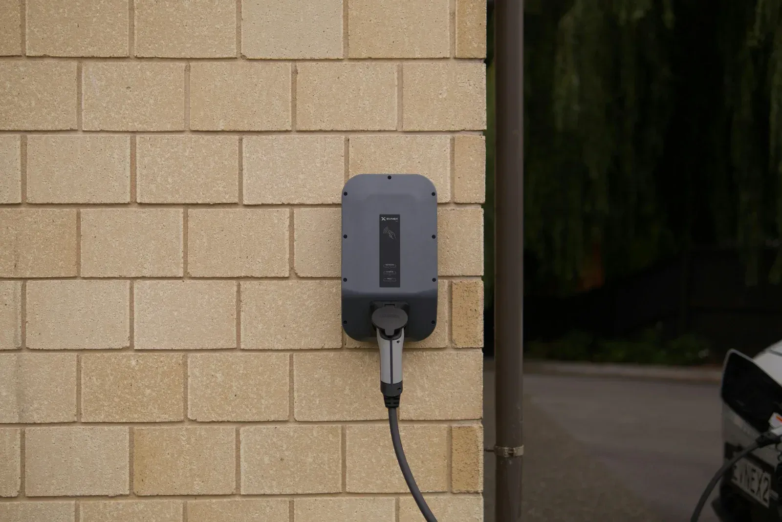 Electric vehicle charger mounted on a brick wall with a charging cable connected.