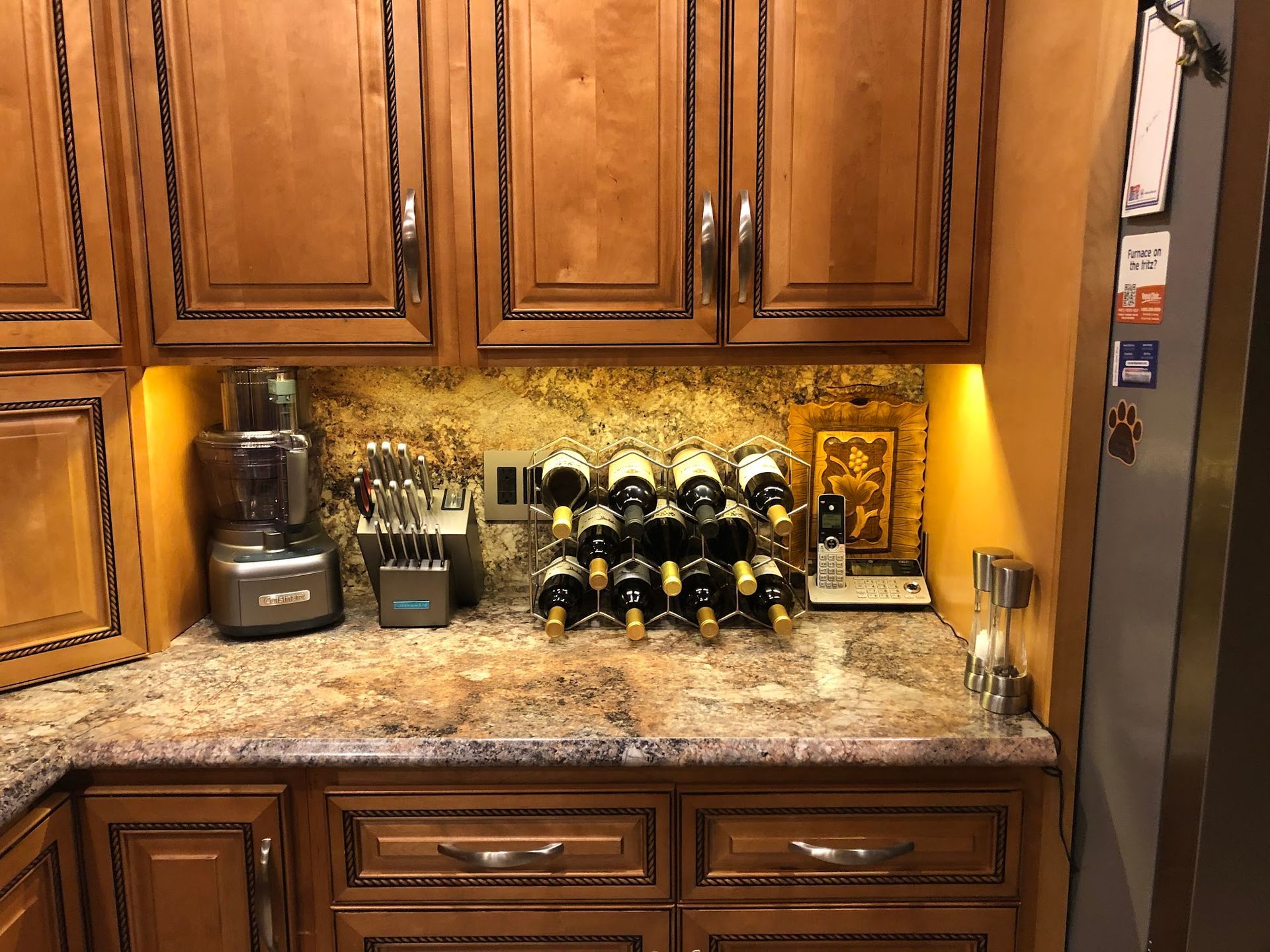 Kitchen cabinet area with wine rack, appliances, and countertop, warm tones.