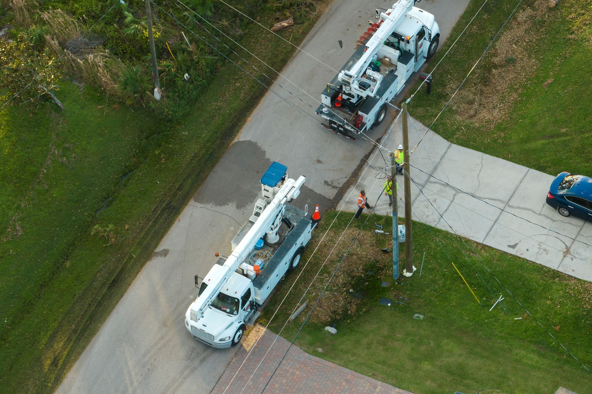 Two utility trucks parked along a grassy roadside near a sidewalk and utility pole.