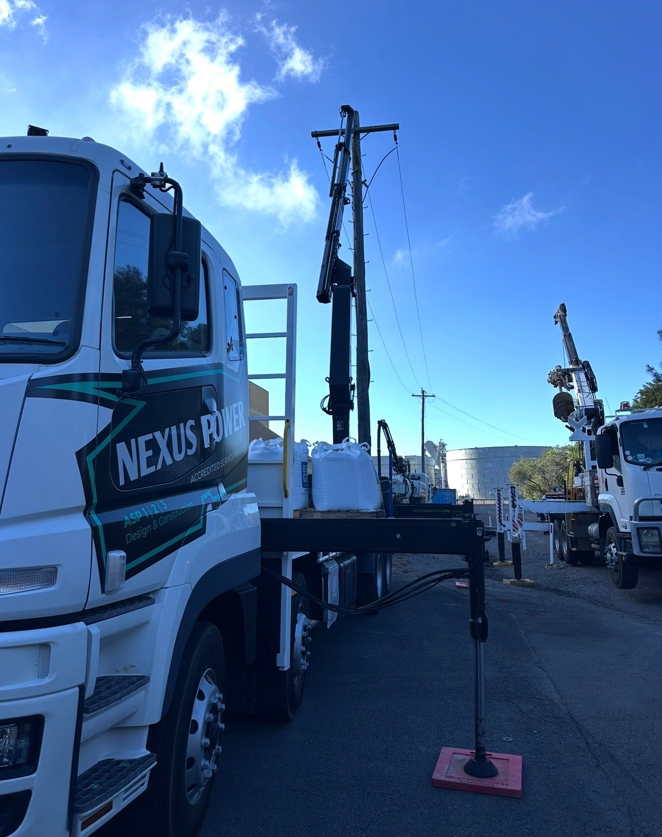 Construction trucks with a drilling rig on a paved lot under a bright blue sky