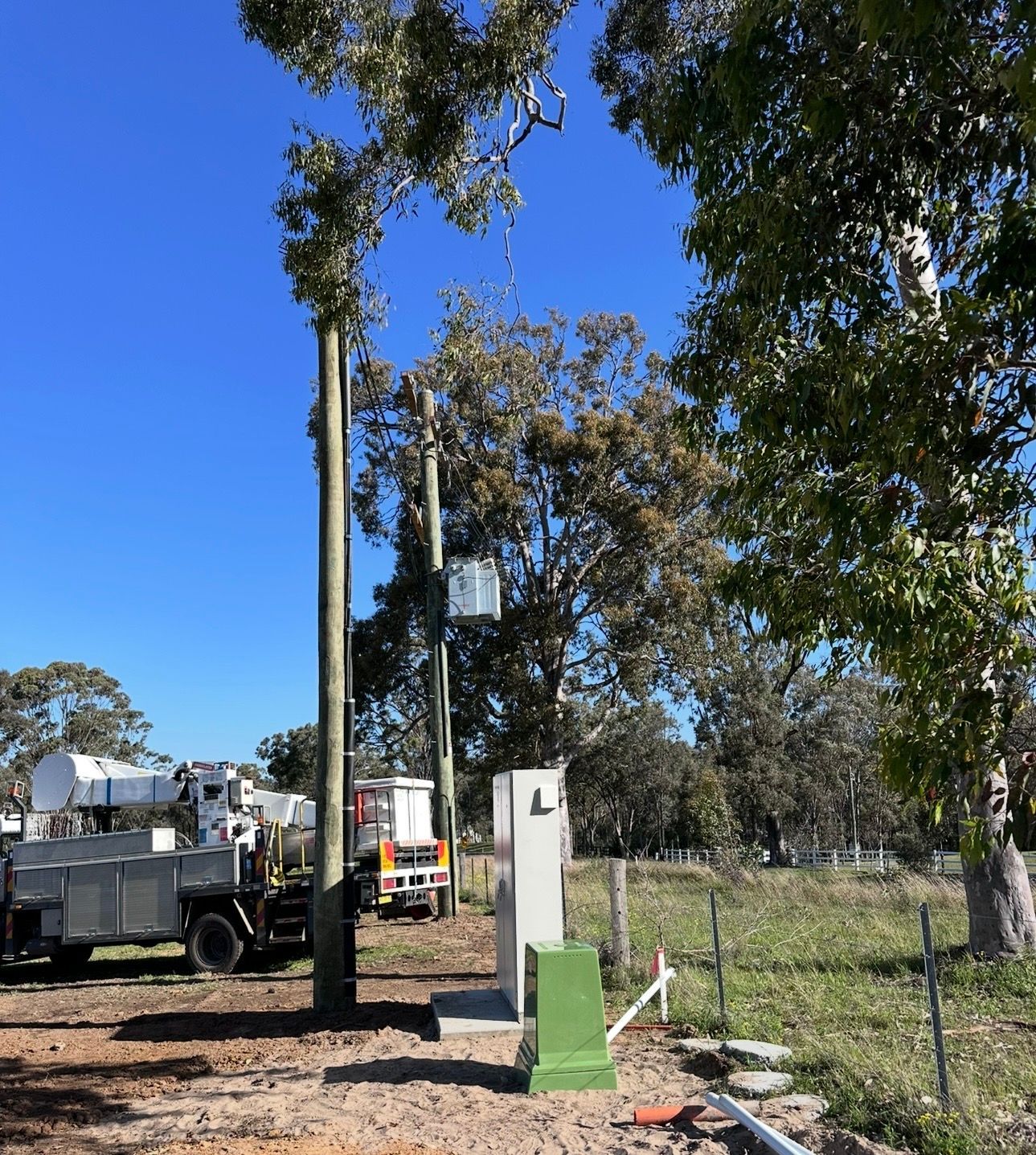 Utility truck beside a green-and-white post in a fenced, tree-lined rural area