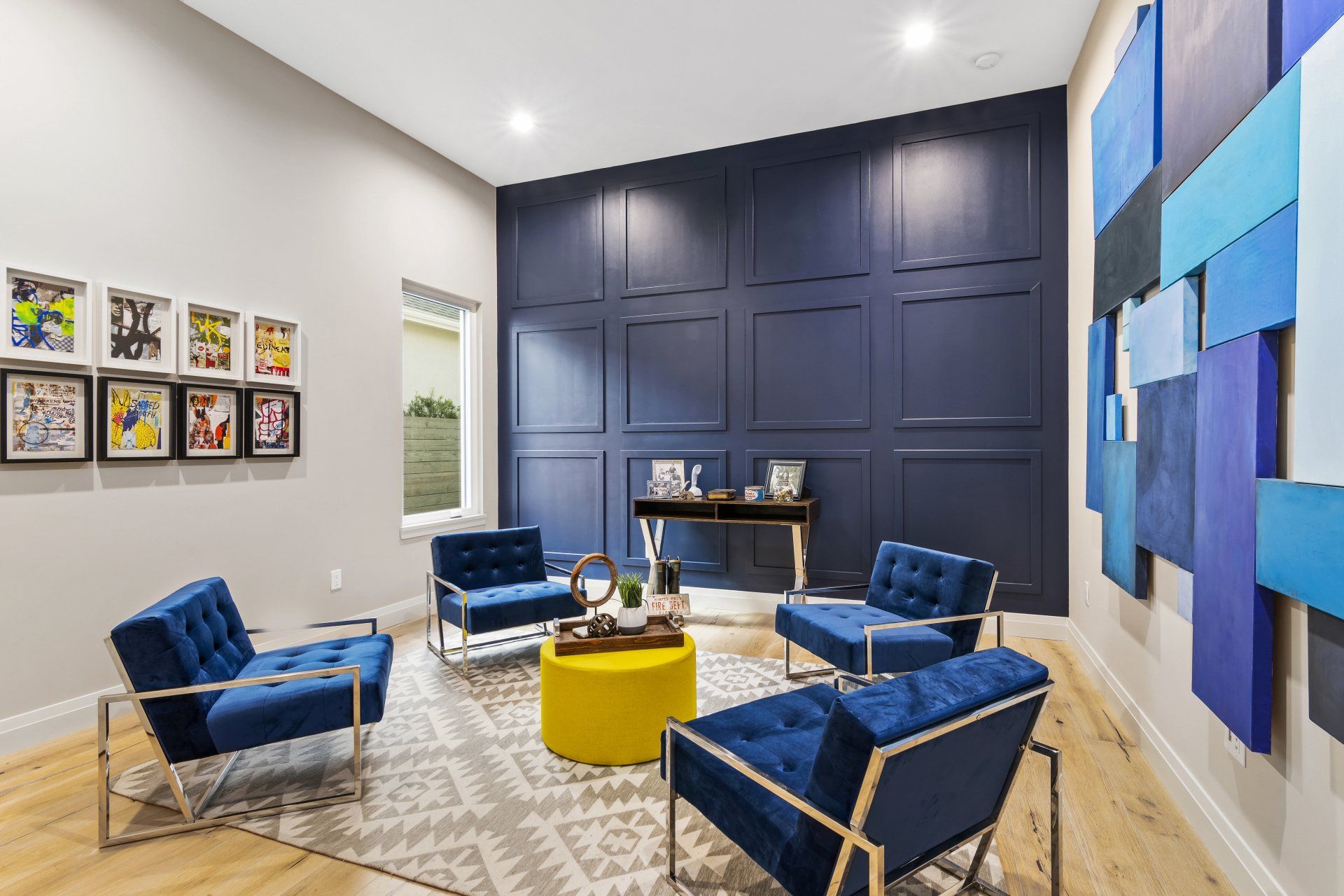 A living room with blue chairs , a yellow table , and a blue wall.