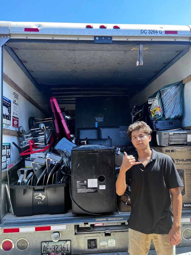 A man is standing in front of a moving truck filled with lots of electronics.