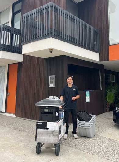 Person standing beside a cart outside a dark wood building with a balcony