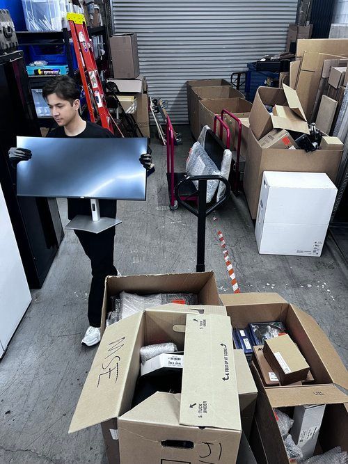 A man is carrying a flat screen tv in a warehouse