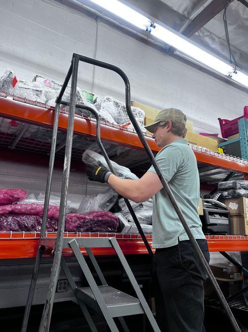 A man is standing on a ladder in a warehouse.