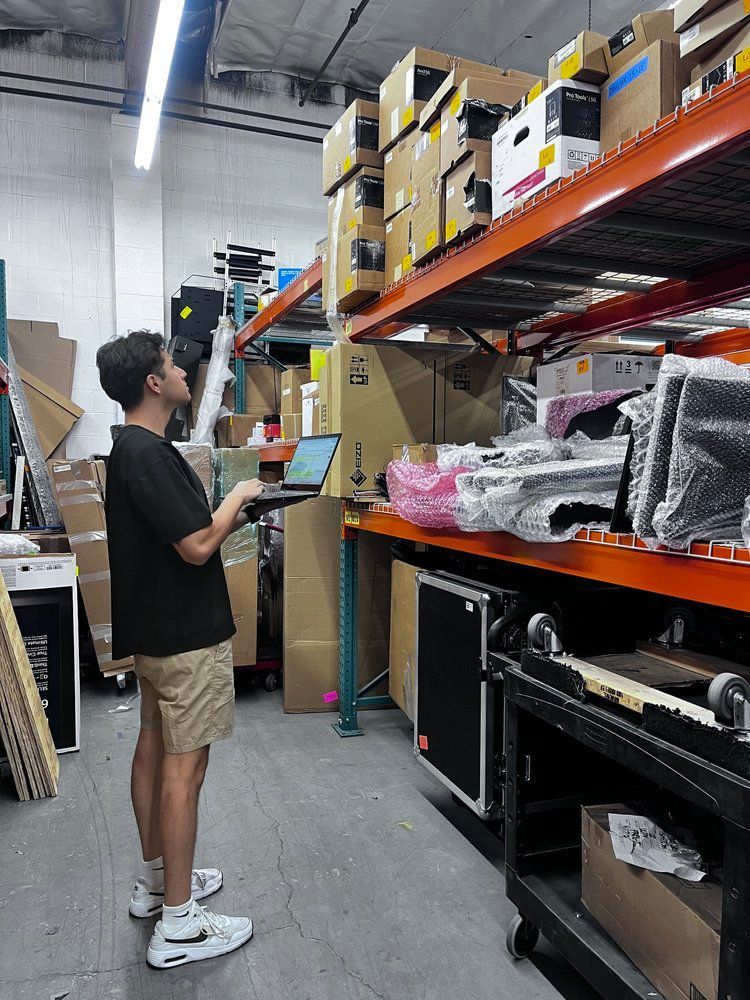 A man is standing in a warehouse looking at a laptop