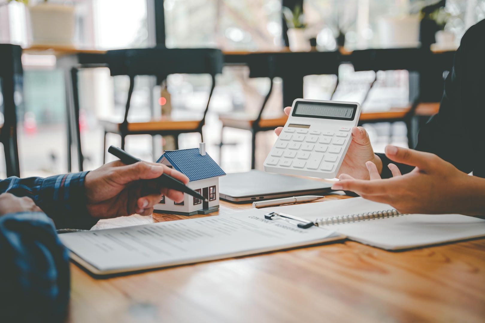 A person is sitting at a table holding a calculator and a model house.