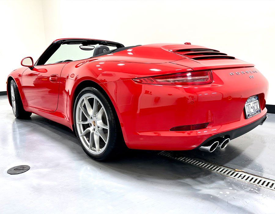 Red convertible Porsche sports car, rear view, silver wheels, on a shiny floor.