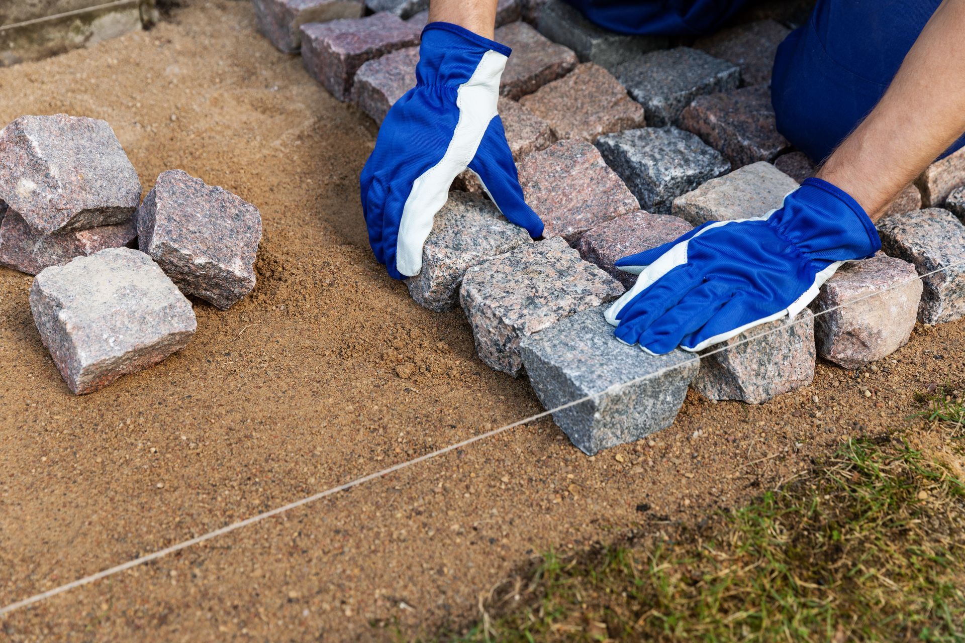 Person in blue gloves laying stone pavers on sand.