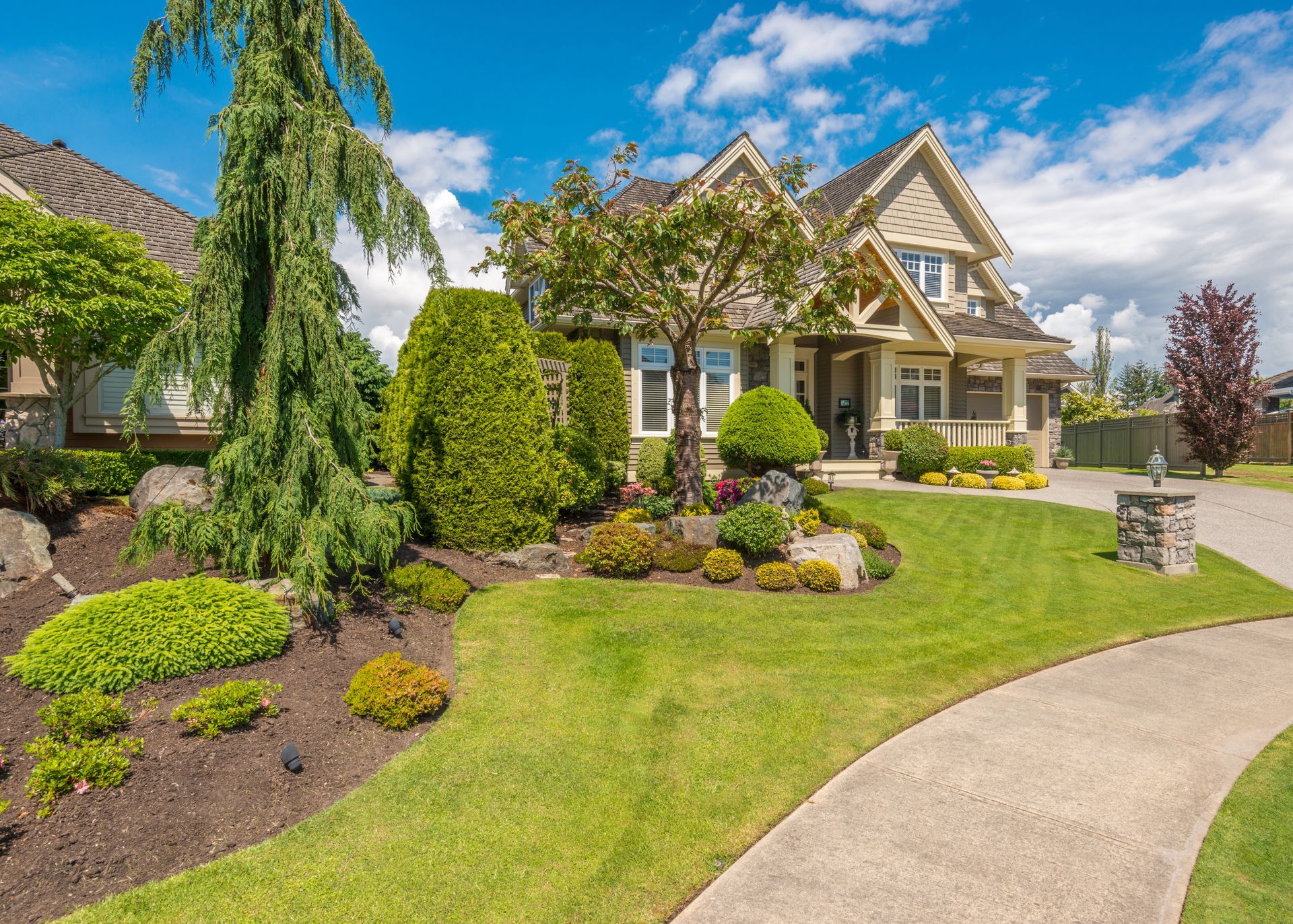 Well-manicured house with a stone pathway, lush green lawn, and vibrant landscaping under a blue sky.