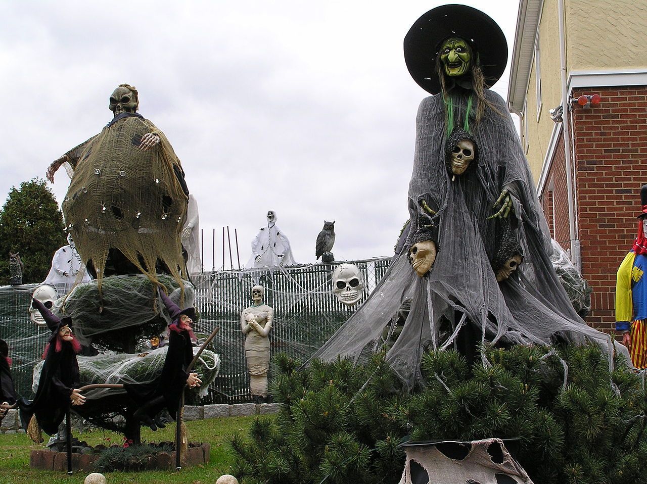 Halloween decorations on a lawn: a giant witch, zombie, skeleton statues, and other spooky figures.