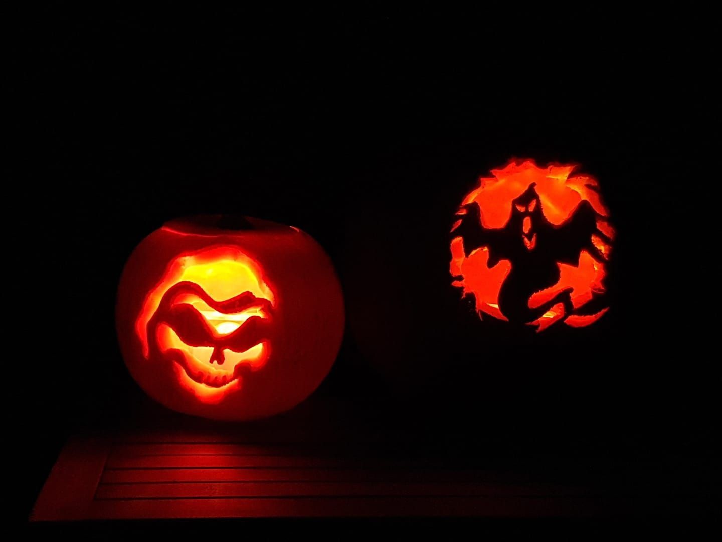 Two lit jack-o-lanterns with spooky faces glow orange in the darkness.