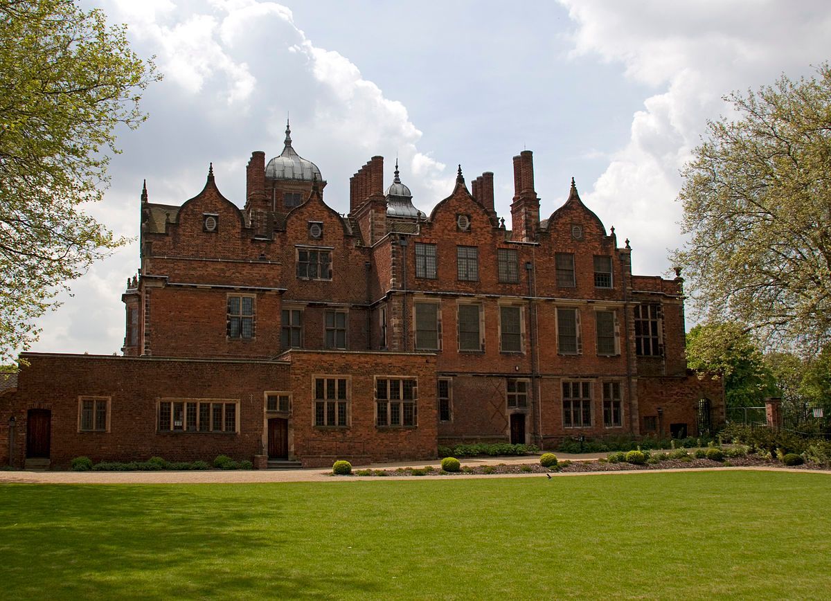 Historic red brick mansion with lawn under a cloudy sky.