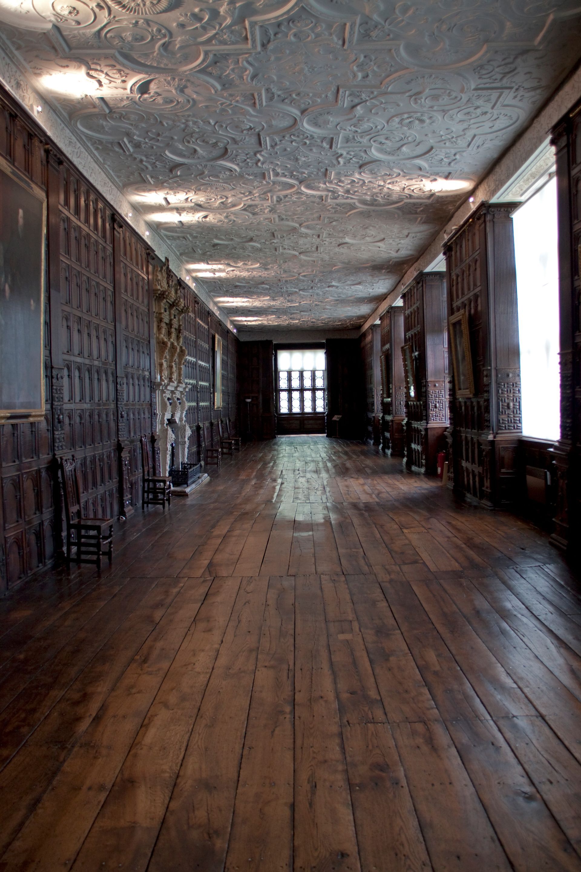 Long, wood-paneled hallway with a patterned ceiling and windows.