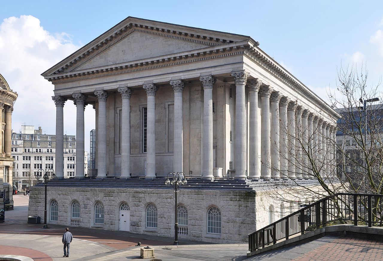 Classical-style building, Birmingham, UK, with large columns, stone facade. Man walks in the square.