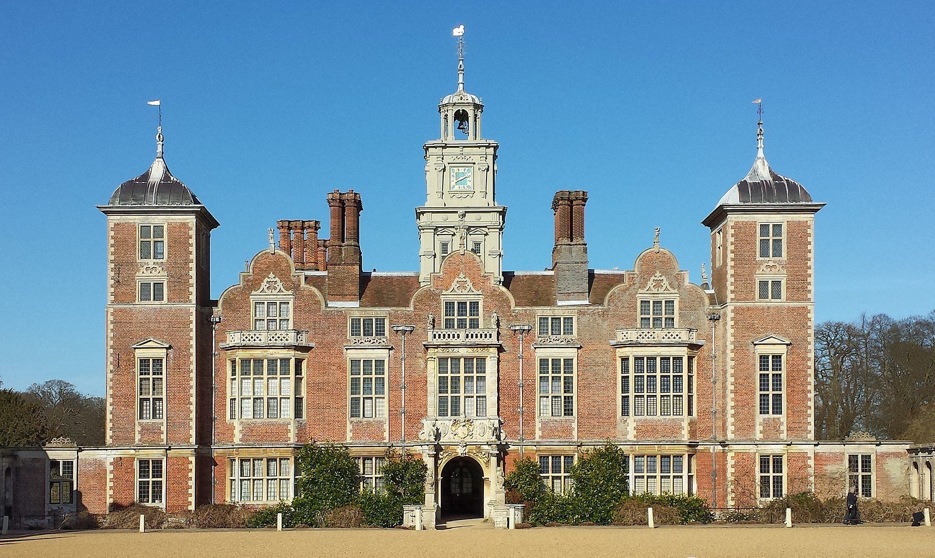 Historic red brick house with a clock tower and turrets against a clear blue sky.