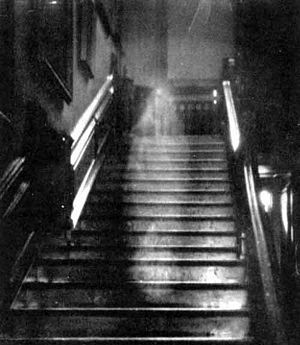 Ghostly figure on a staircase, appears to be walking up steps in a darkened building.