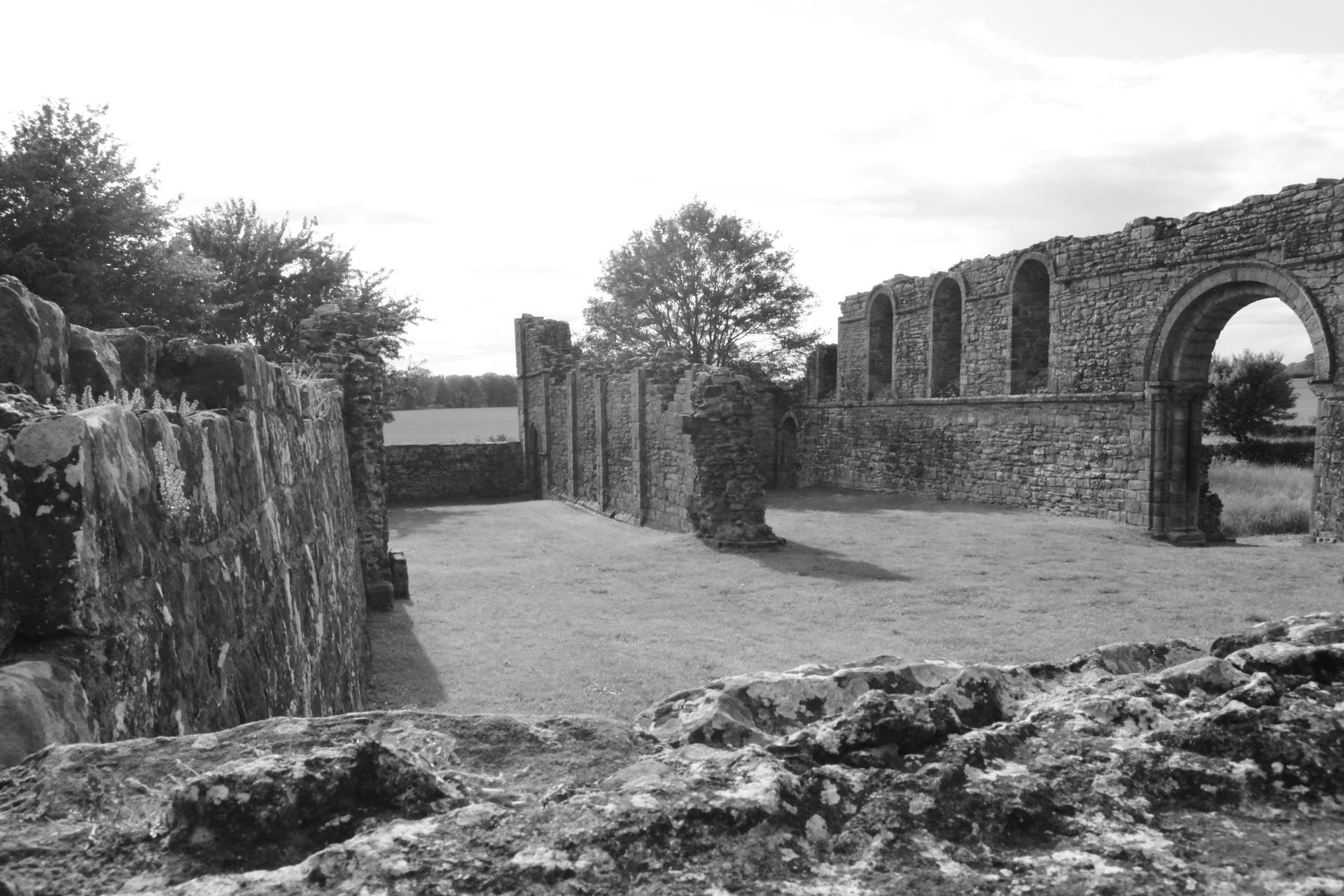 Ruins of stone building with arched windows, open to a grassy courtyard, in an outdoor setting.