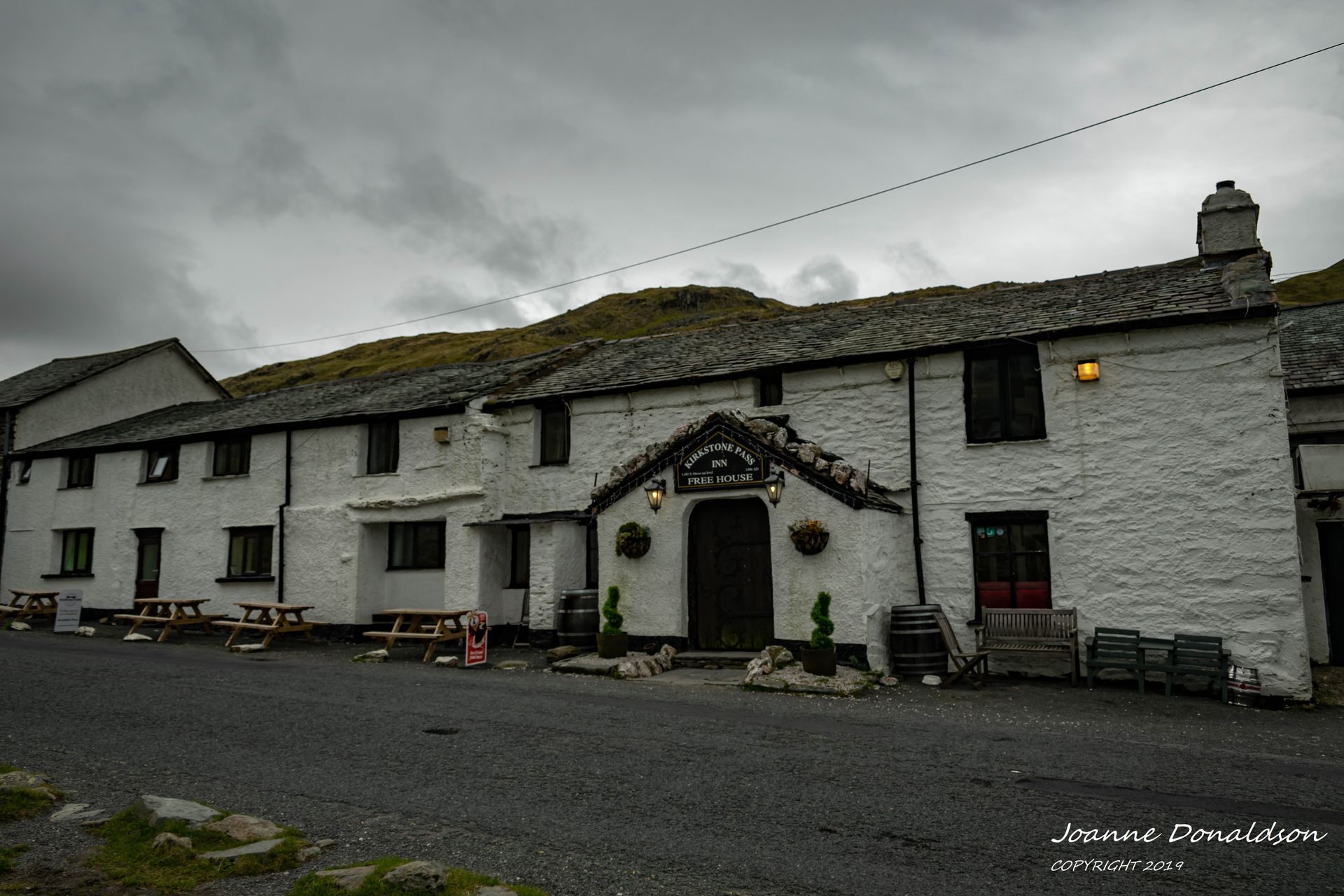 White pub under a cloudy sky in a rural setting. Wooden tables outside.