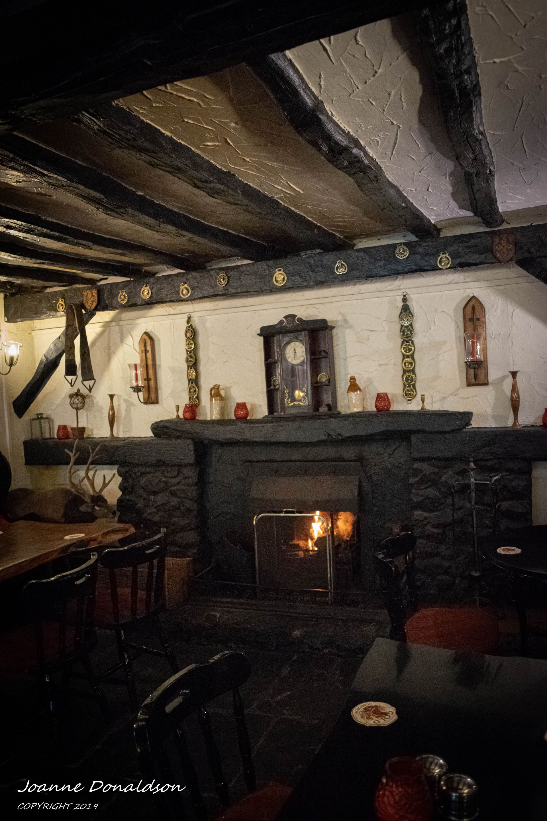 Cozy interior with fireplace, clock, and decorative items in a dark-timbered, rustic setting.