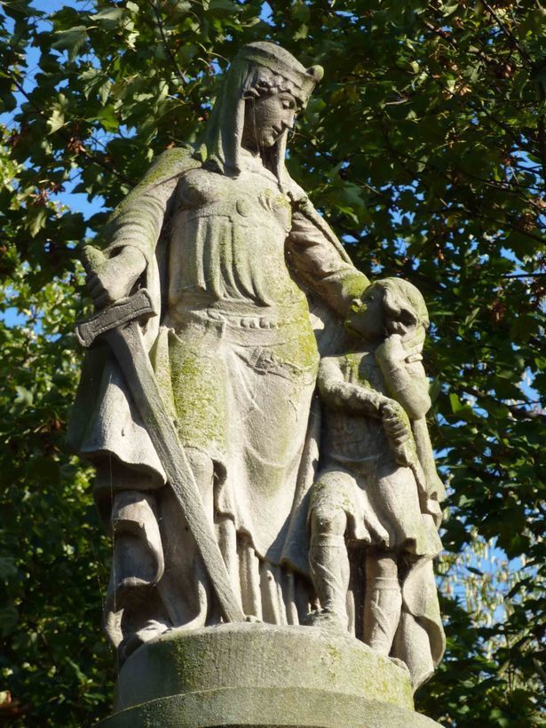 Statue of a woman in a crown and robes holding a sword, guiding a young boy. Outdoors.