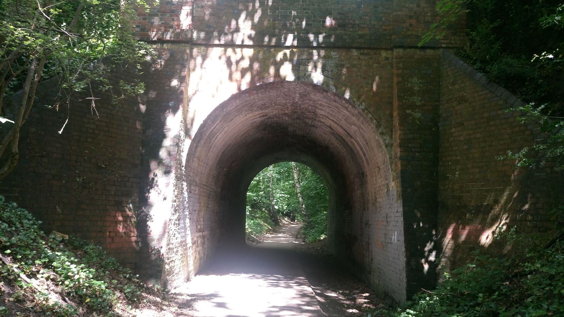 Tunnel entrance, brick archway under a shaded path, sunlight at the end.