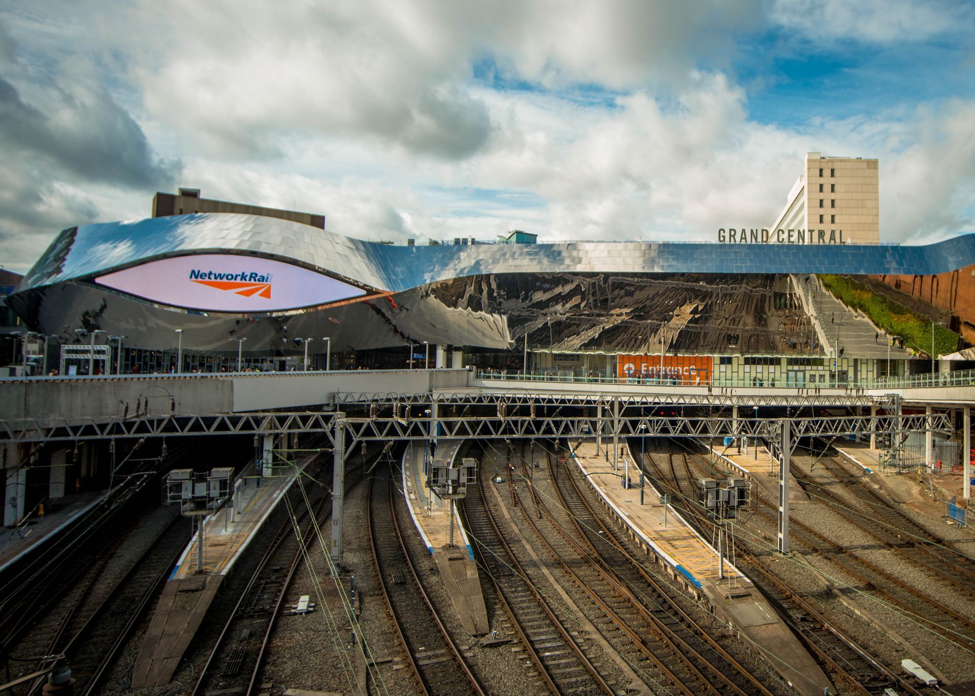 Birmingham New Street Station, UK. Modern station exterior with train tracks, cloudy sky.