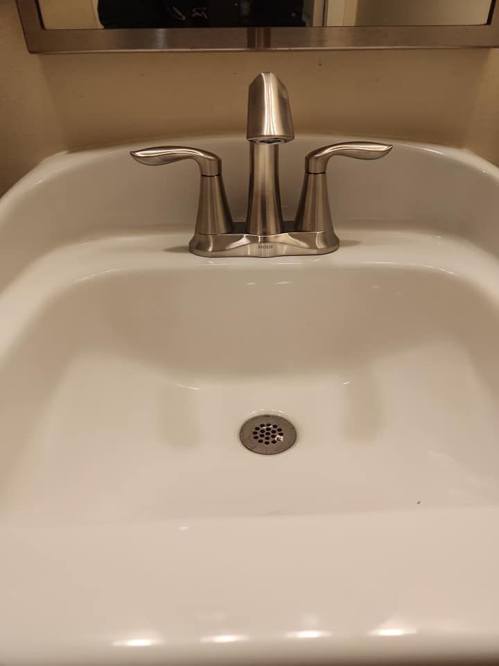 A modern, brushed-nickel bathroom faucet centered over a white ceramic sink basin with a drain grate.