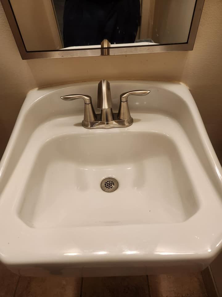 A top-down view of a white, wall-mounted bathroom sink with a silver, two-handle faucet and a mirror above.