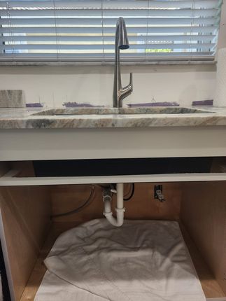 Kitchen sink with a tall silver faucet, granite countertop, and open cabinet base revealing white plumbing pipes.
