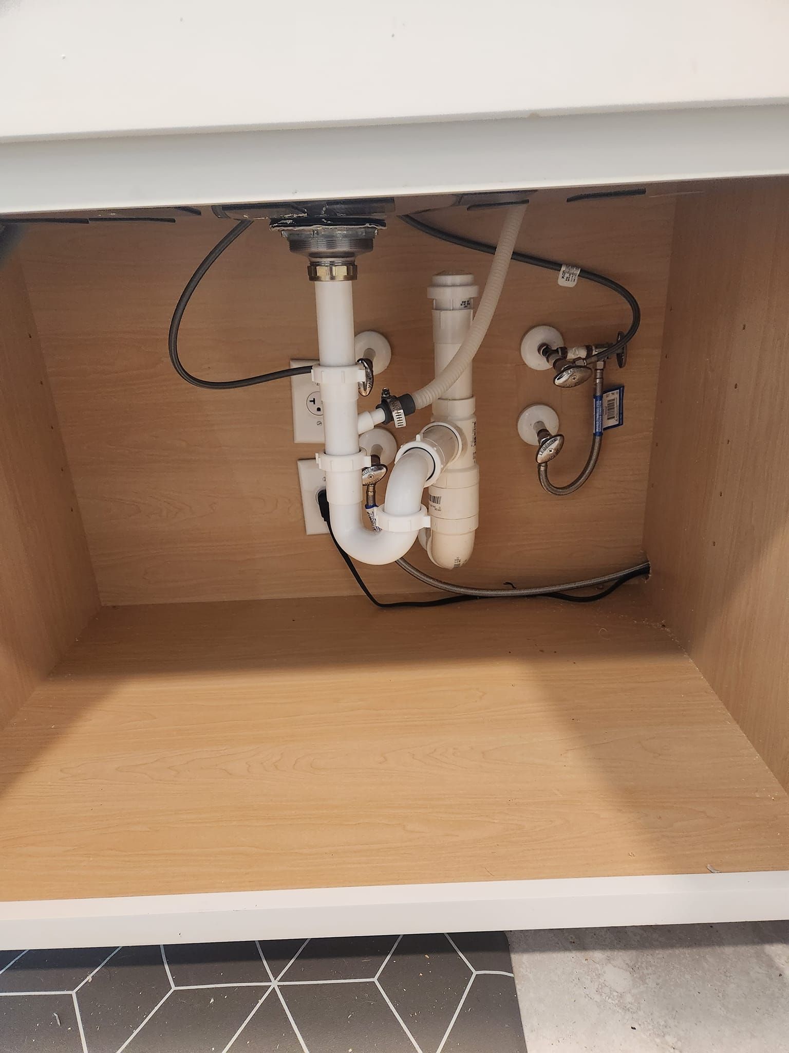 Interior view of a bathroom vanity cabinet showing white plumbing pipes and water supply valves under a sink.