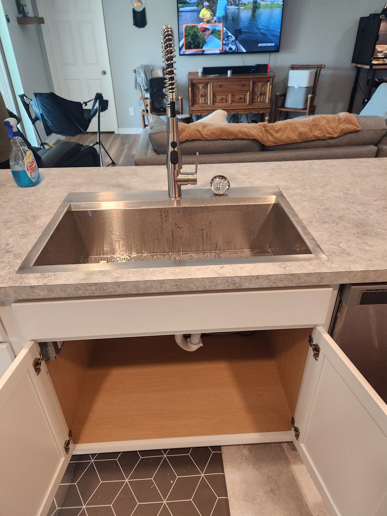 A kitchen island sink with an open base cabinet below, featuring a tall faucet and light-colored granite countertop.
