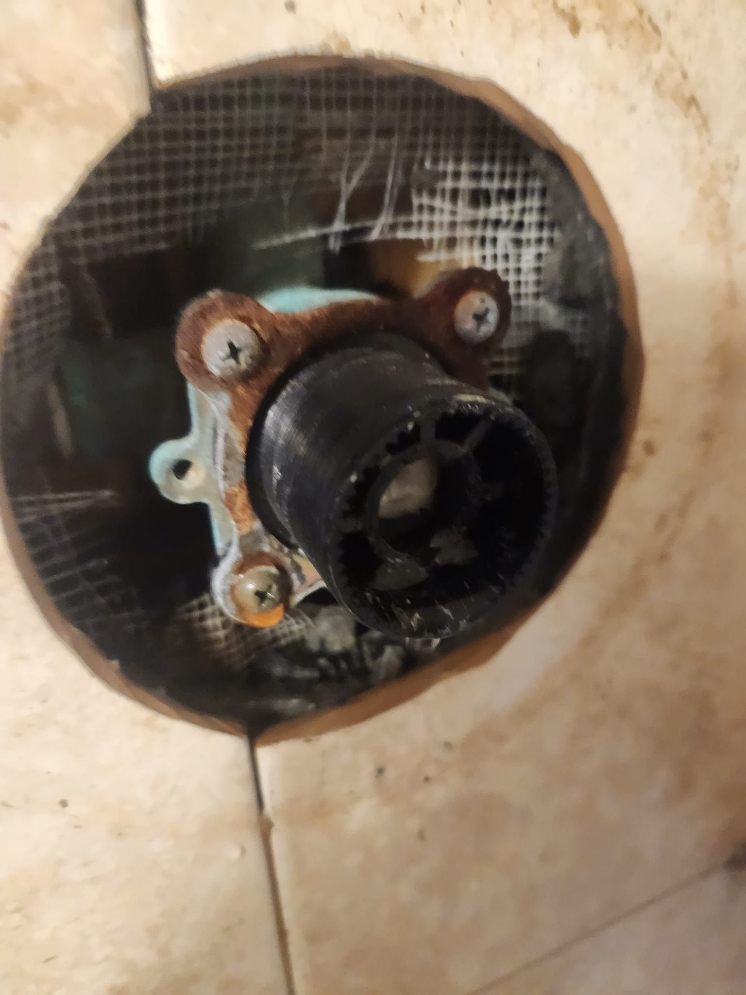 A close-up view of a recessed shower faucet valve body with a black plastic cartridge installed in a tiled wall.