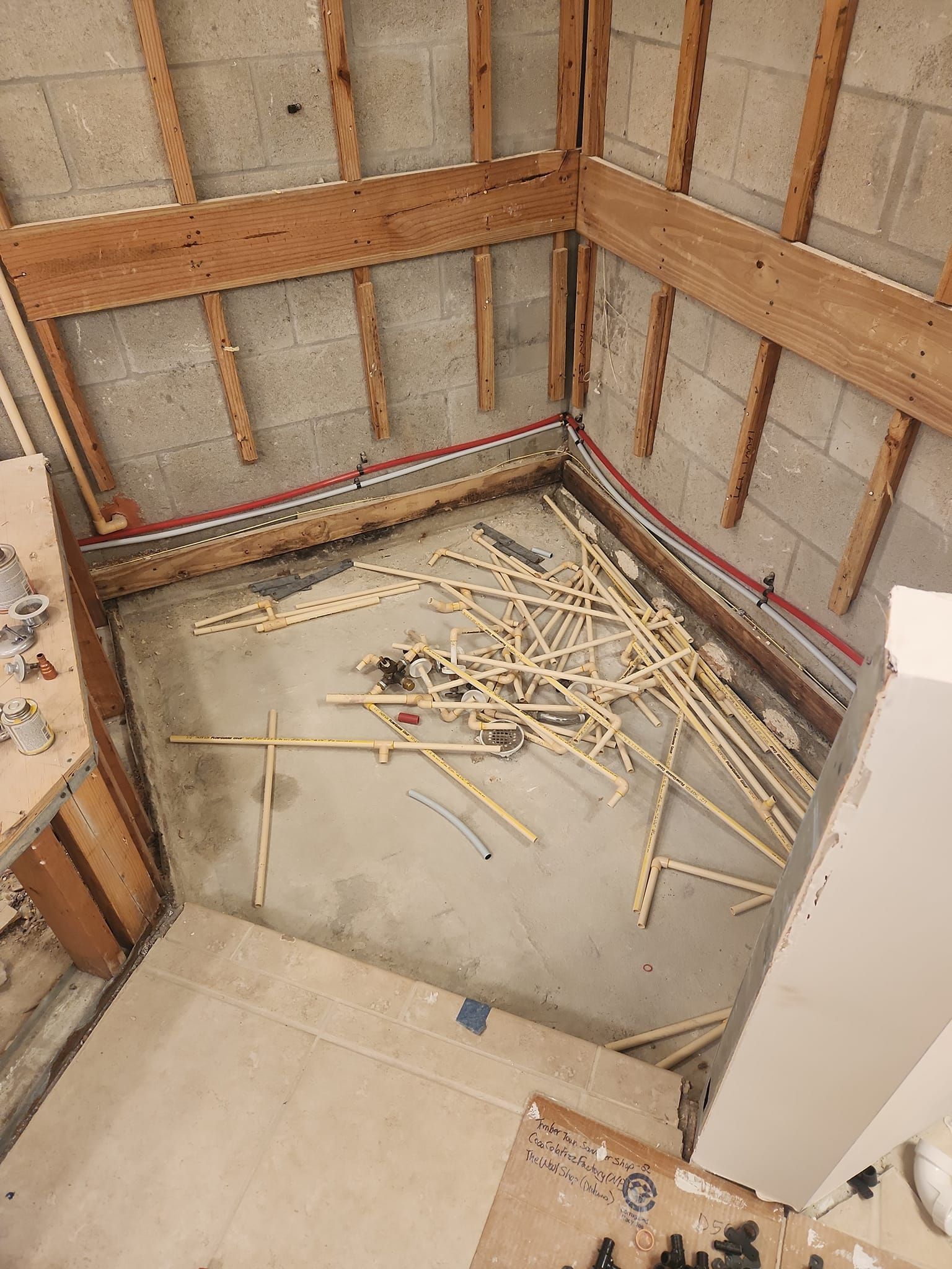 A corner space under construction with concrete block walls, wooden wall framing, and construction debris on the floor.