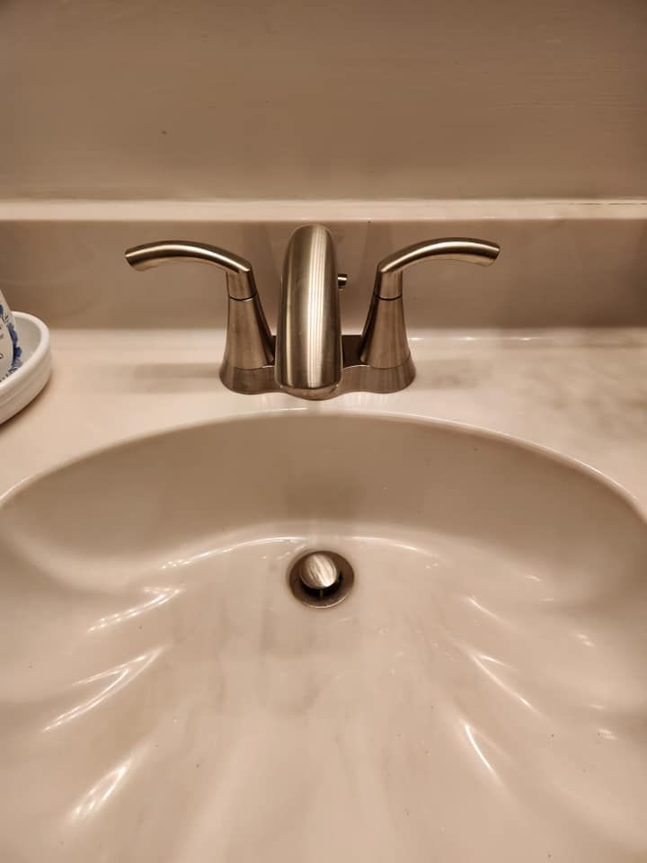 A stainless steel, two-handle bathroom faucet mounted on a white, shell-shaped pedestal sink.