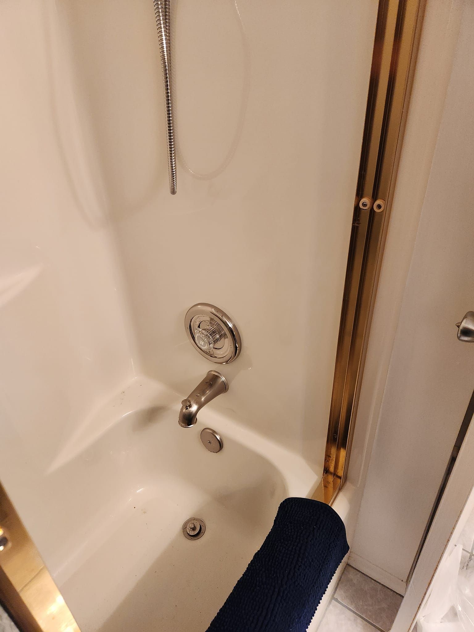 A white shower and bathtub unit with a chrome faucet, handle, and a dark blue bath mat on the edge.